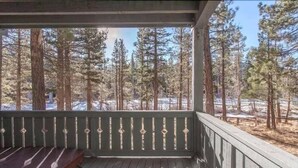 Una terraza de madera con barandilla, con vistas a una zona boscosa de árboles altos y suelo cubierto de nieve.