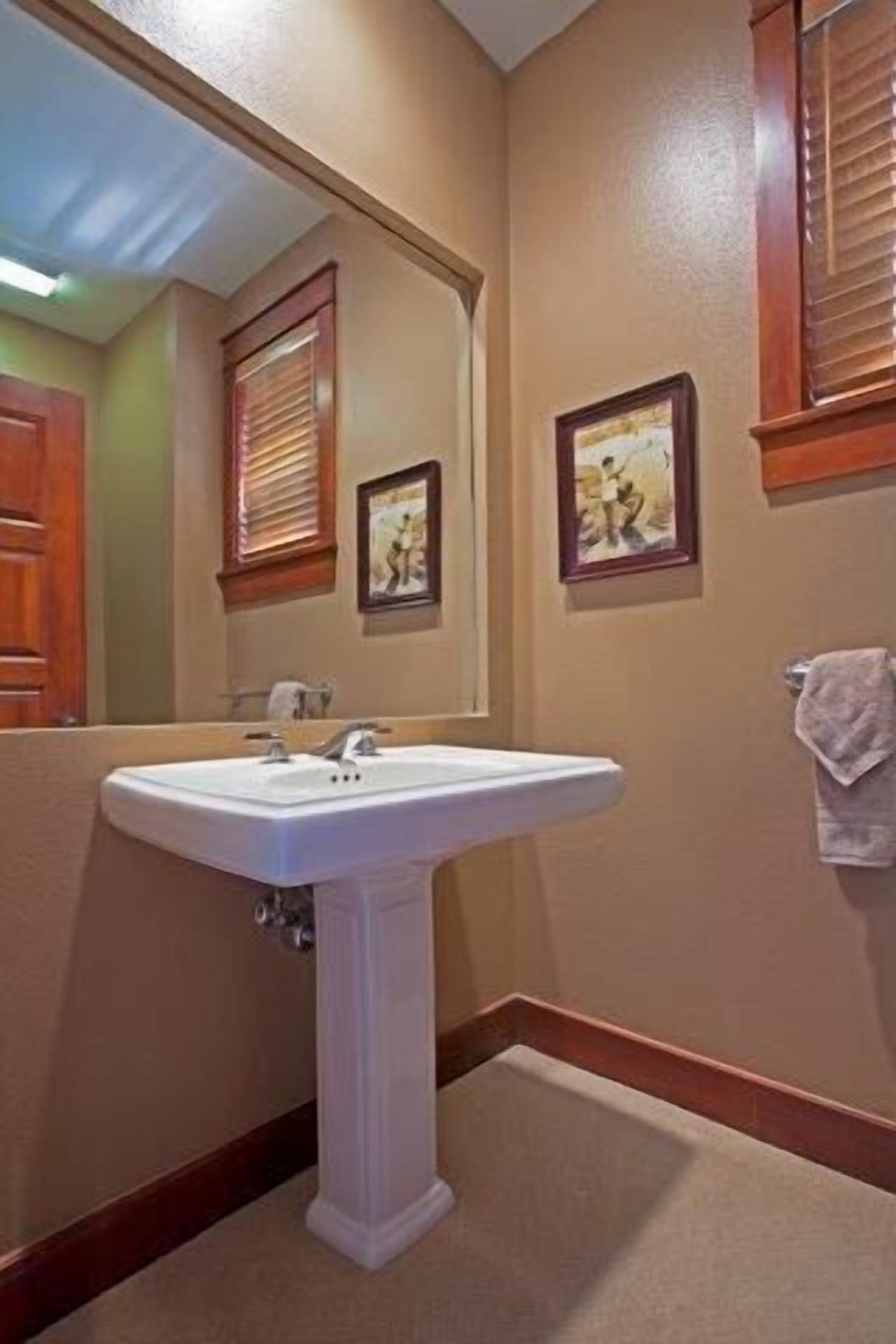 Een badkamer met een wastafel op een zuil, houten lambrisering en ingelijste foto's aan de muur.