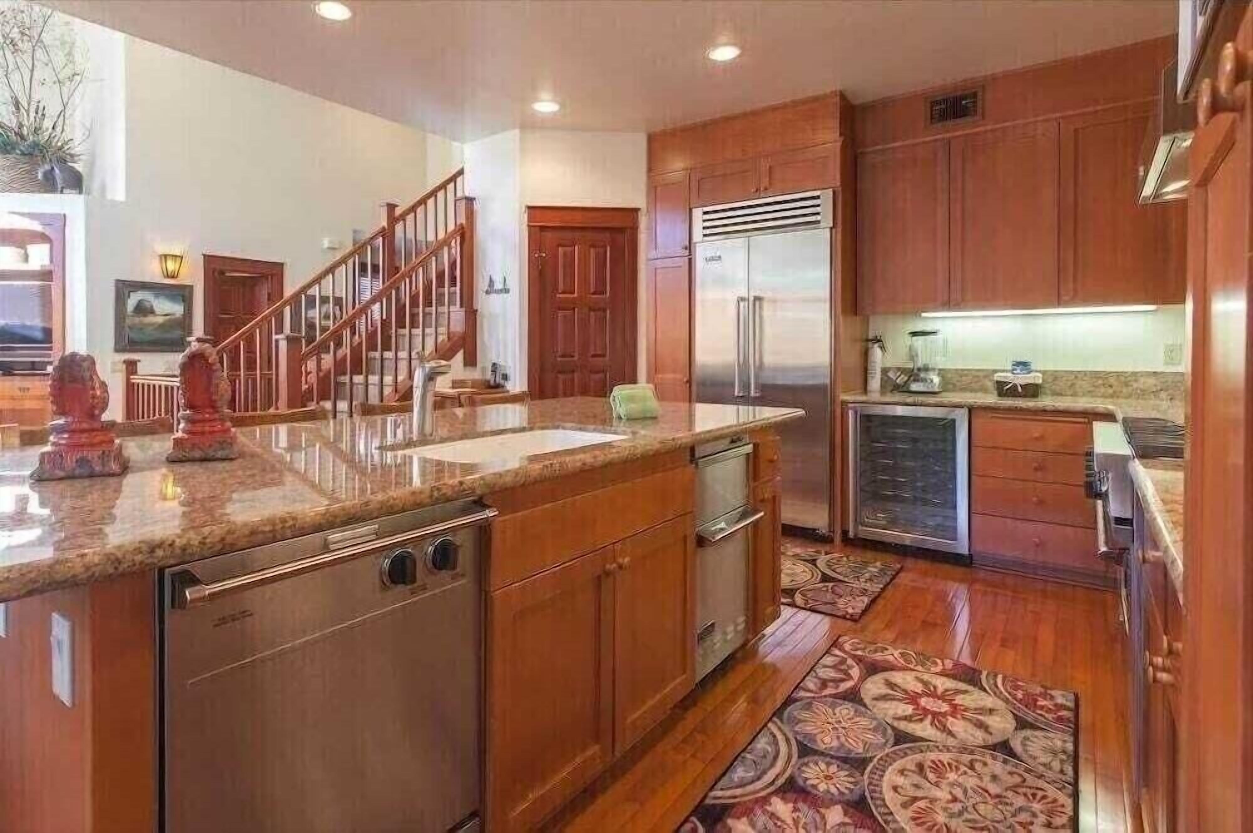 A spacious kitchen with wooden cabinets, a stainless steel refrigerator, and a granite countertop.