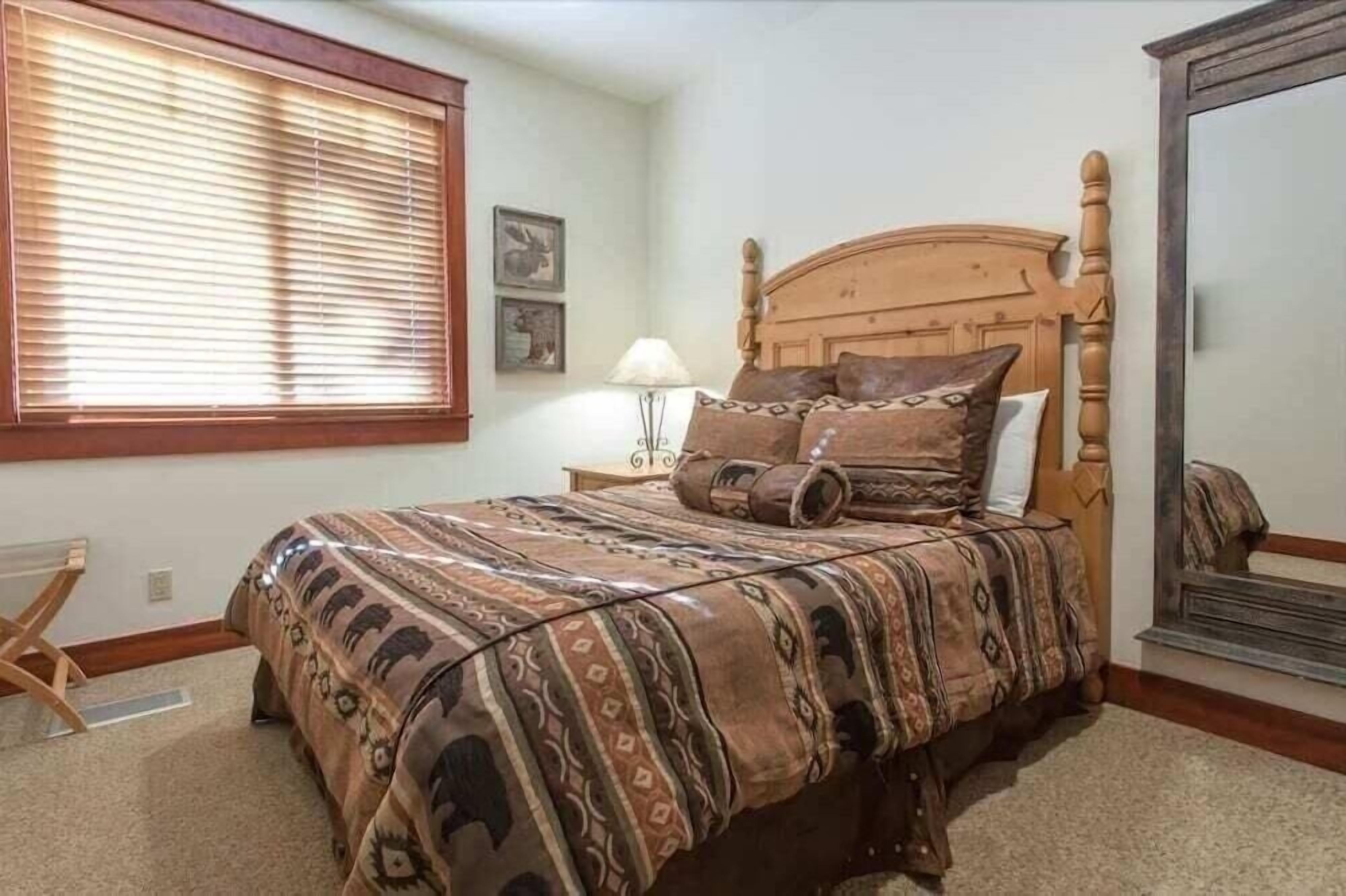 Une chambre à coucher avec un lit en bois, une couvre-lit à motifs, une table de chevet avec une lampe et une fenêtre avec des stores.
