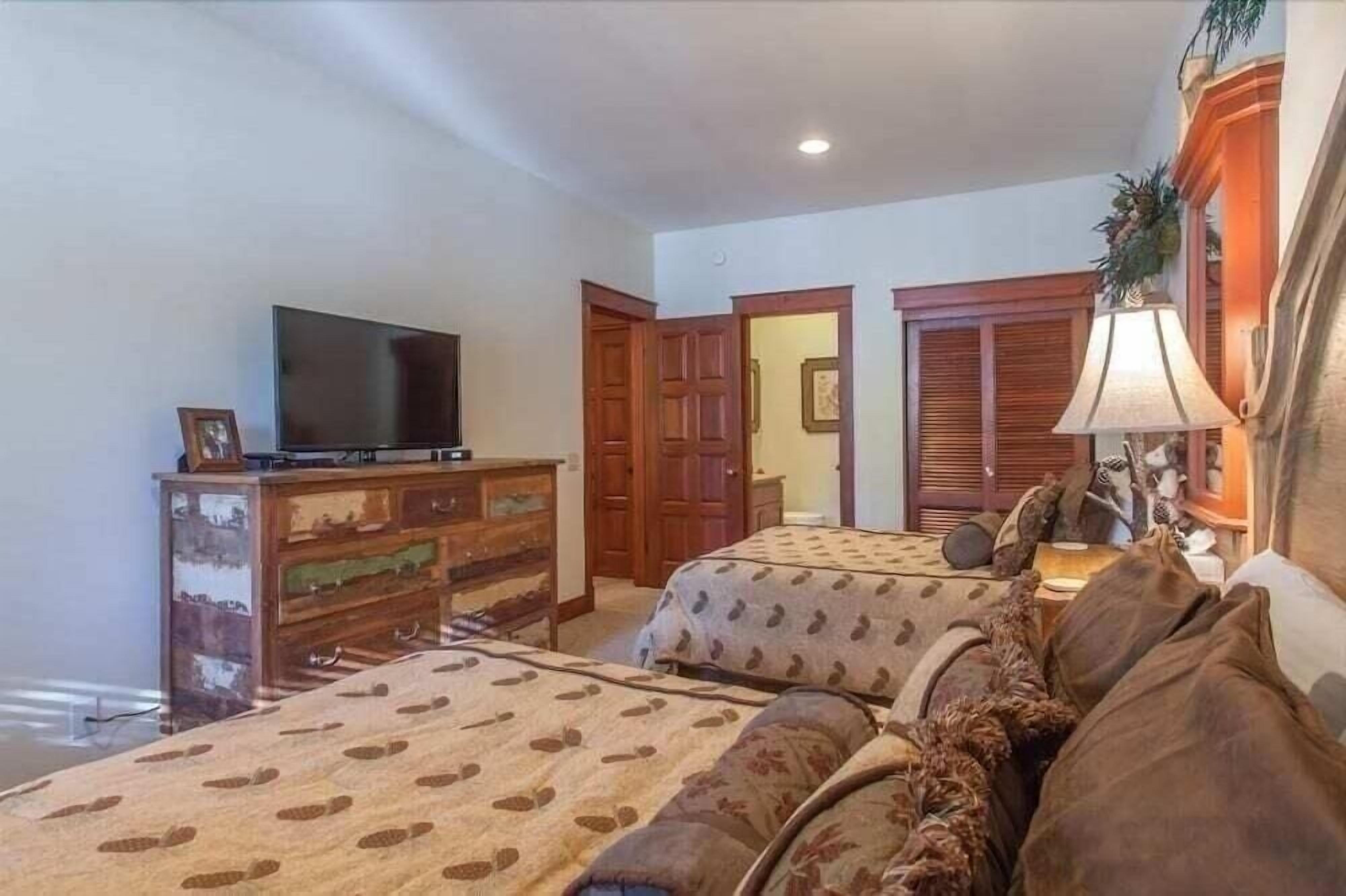 A bedroom with two beds, a dresser, a television, and a lamp.