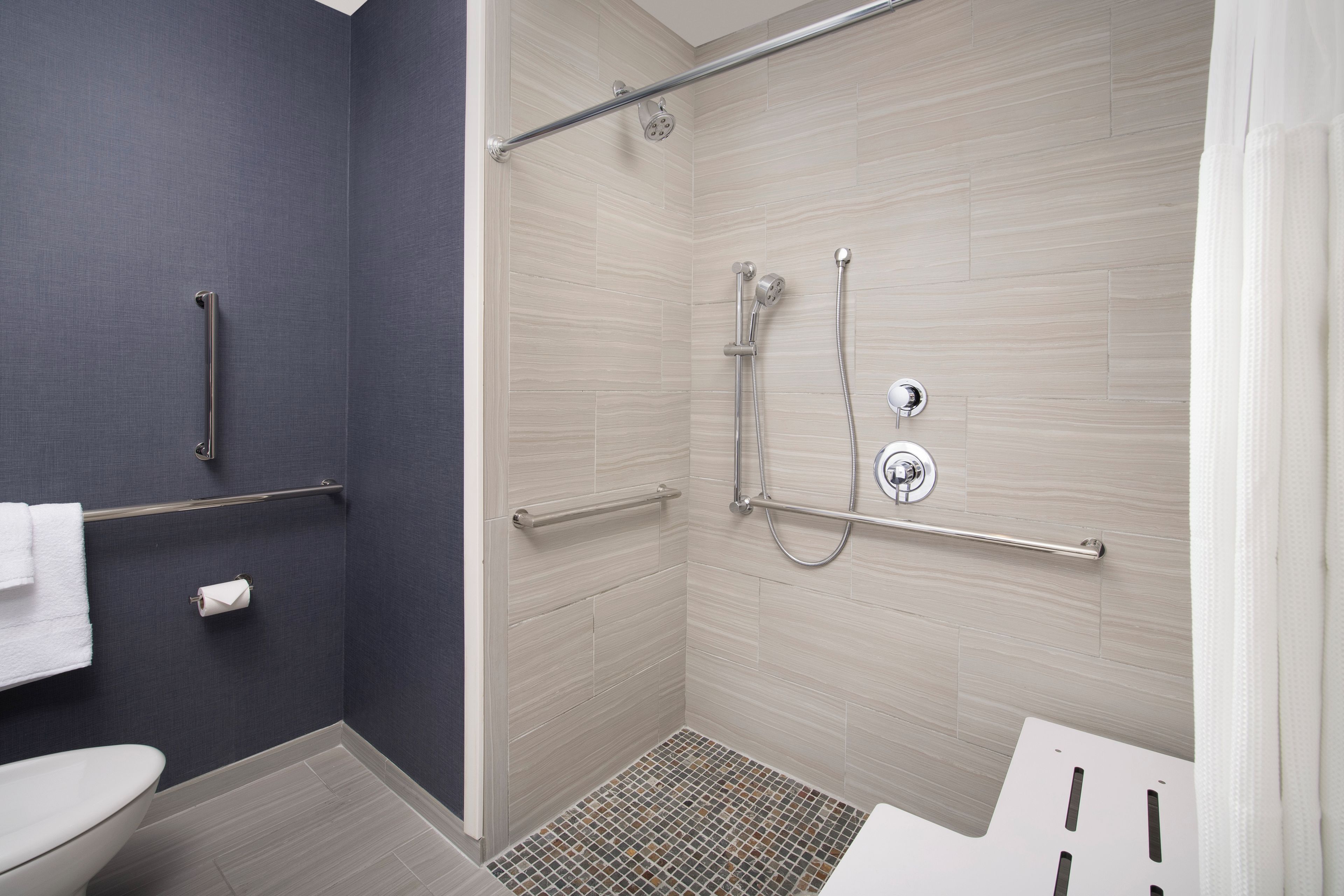 Un baño moderno con ducha, inodoro y barras de apoyo.