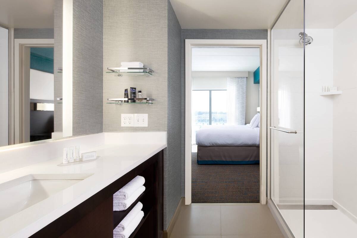 A modern bathroom with a large mirror, white sink, and glass shower enclosure.
