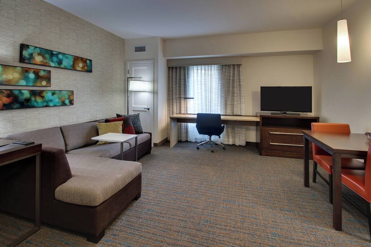 A hotel room with a sofa, a desk, a television, and artwork on the wall.