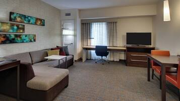 A hotel room with a sofa, a desk, a television, and artwork on the wall.