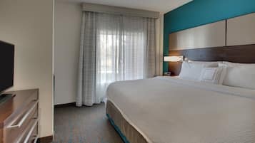 Una habitación de hotel con una cama grande, un televisor en un aparador de madera y una ventana con cortinas traslúcidas.