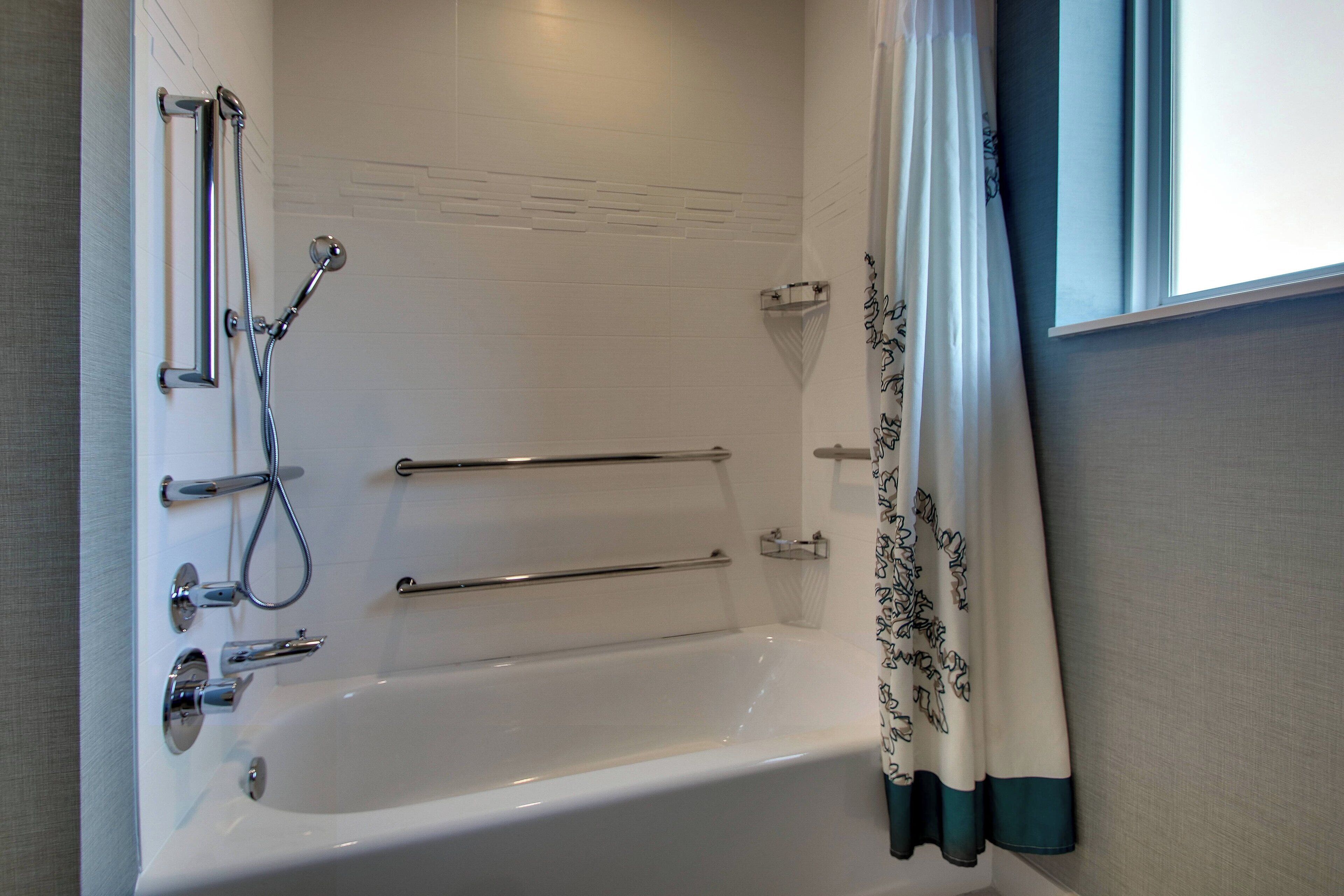 A bathroom with a white bathtub, chrome fixtures, and a shower with a handheld showerhead.
