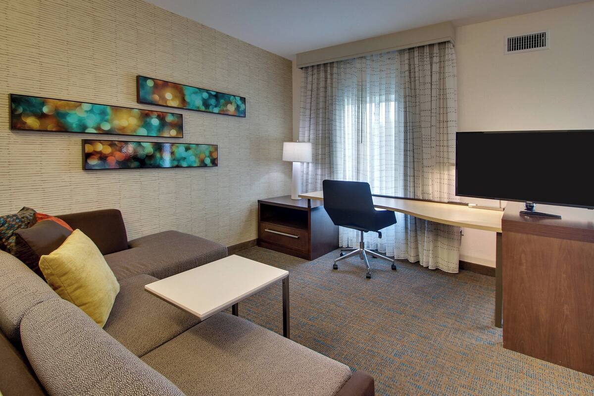 A hotel room with a sofa, a desk, a television, and three abstract paintings on the wall.