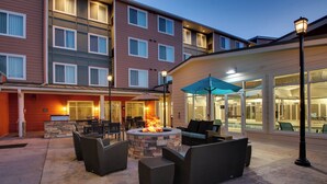 An outdoor patio with wicker furniture, a stone fire pit, and a glass-enclosed building in the background. - Residence Inn Valley Forge/Collegeville (Collegeville)