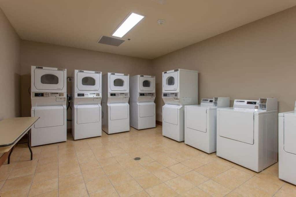 A laundry room with multiple washing machines and dryers, a table, and a ceiling light.