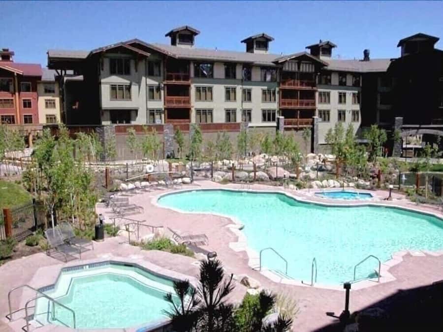 Un hotel con una grande piscina esterna, diversi balconi e una zona verde con rocce e alberi.
