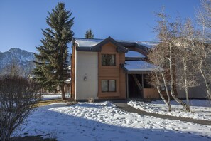 A two-story log cabin with a snow-covered roof and a mountain backdrop.