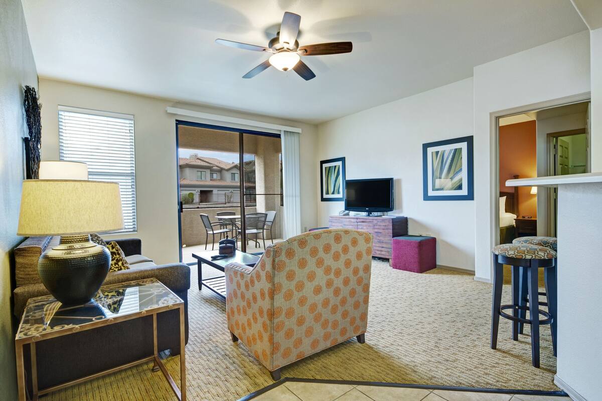 A living room with a ceiling fan, a sofa, a coffee table, a TV, and a dining area with chairs and a table.