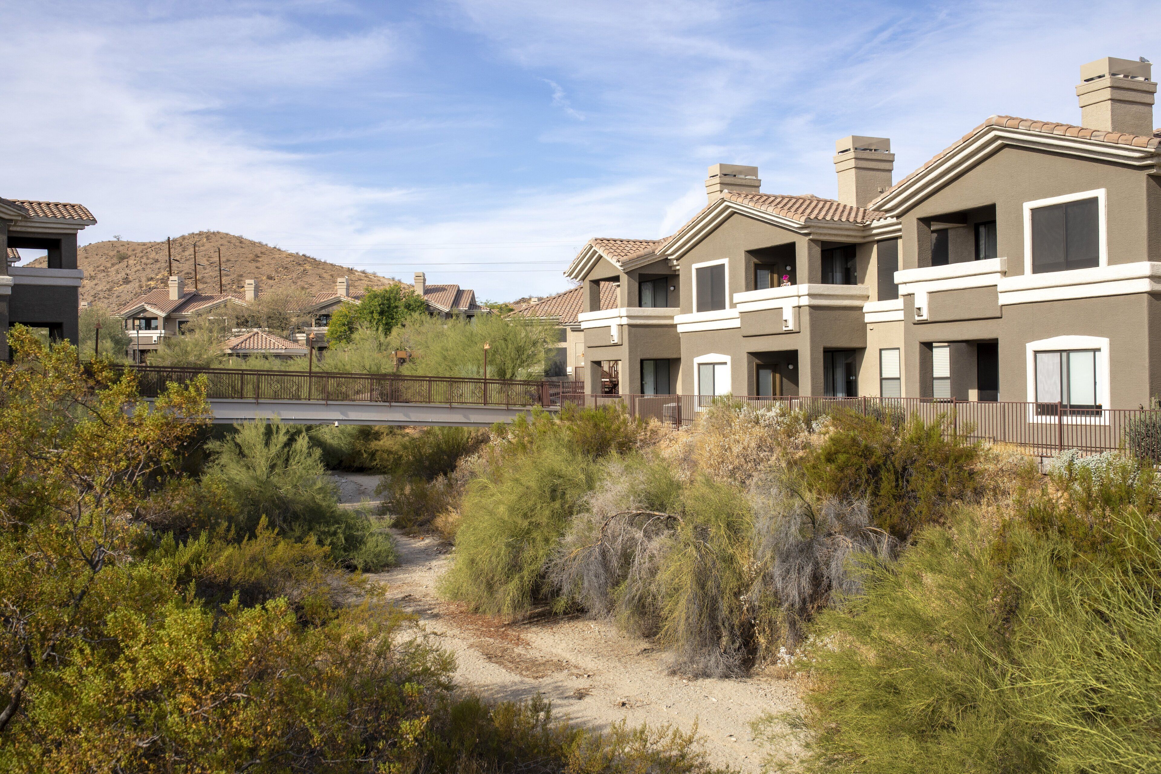 A residential area with modern houses, a dirt path, and a hilly landscape in the background.