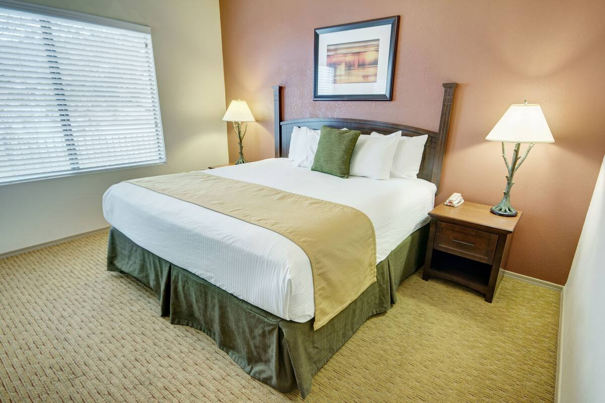 A neatly made bed with a green skirt, two bedside lamps, and a framed picture on the wall.