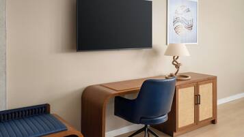 Une chambre moderne avec un bureau en bois, une chaise bleue, un téléviseur fixé au mur et une petite armoire avec une lampe.