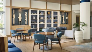 A modern lounge area with round tables, blue chairs, and a bookshelf with decorative items. - Maritime Hotel Fort Lauderdale Airport & Cruiseport (Fort Lauderdale)