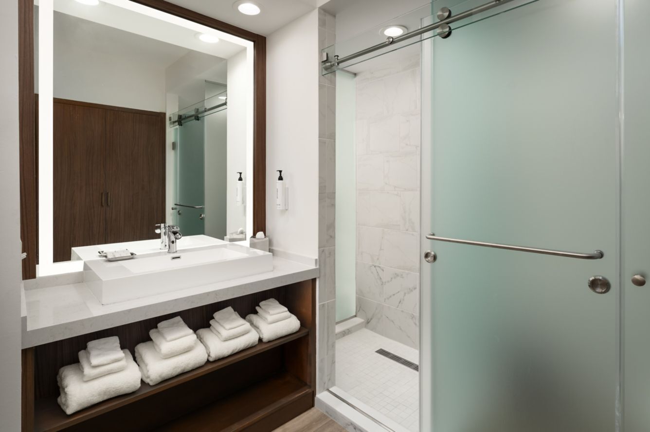 Un baño moderno con un espejo grande, un lavabo blanco y una ducha con mampara de vidrio.
