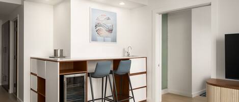 A modern kitchen with a built-in refrigerator, two bar stools, and a wall-mounted artwork.