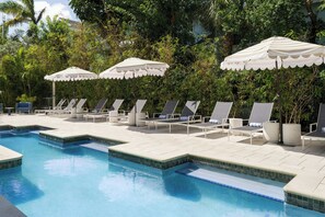 Un espace piscine agrémenté de chaises longues et de parasols, le tout entouré de verdure.