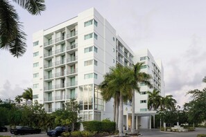 Un hôtel à plusieurs étages doté de balcons, d’un parking couvert et de palmiers.