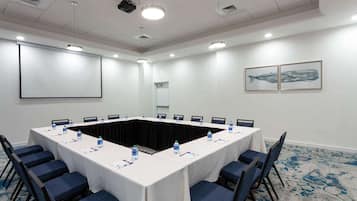 Una sala conferenze con un lungo tavolo, sedie, uno schermo per proiettore e un erogatore d'acqua.