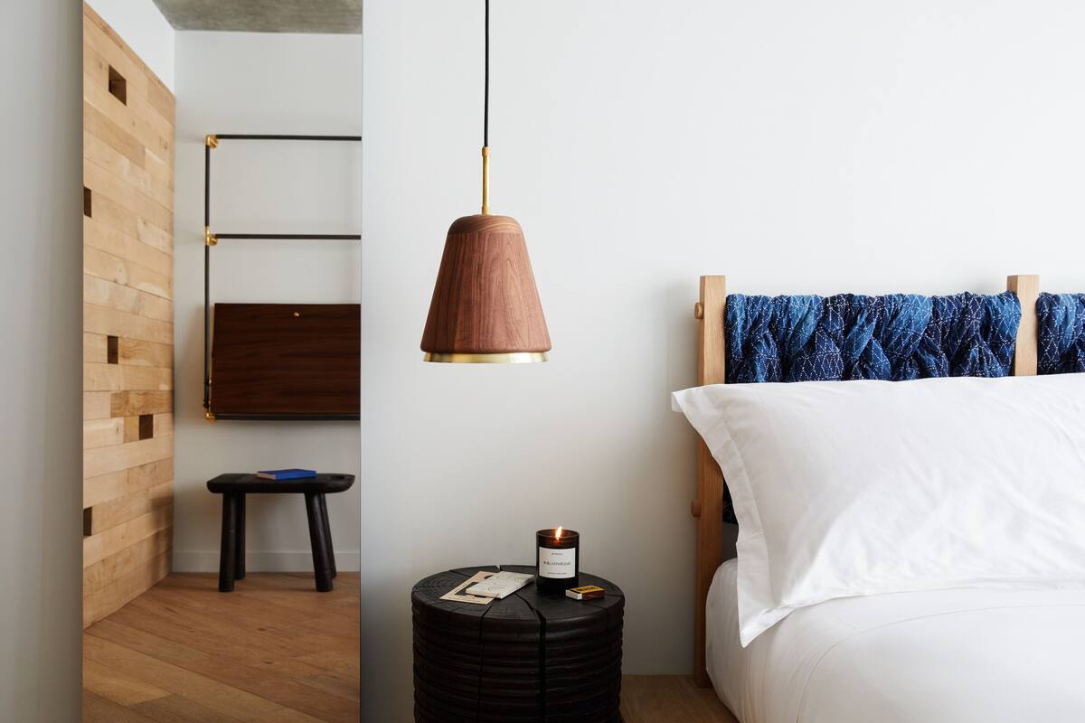Un dormitorio con cabecera de madera, una mesita de noche redonda negra con una vela y una lámpara colgante.