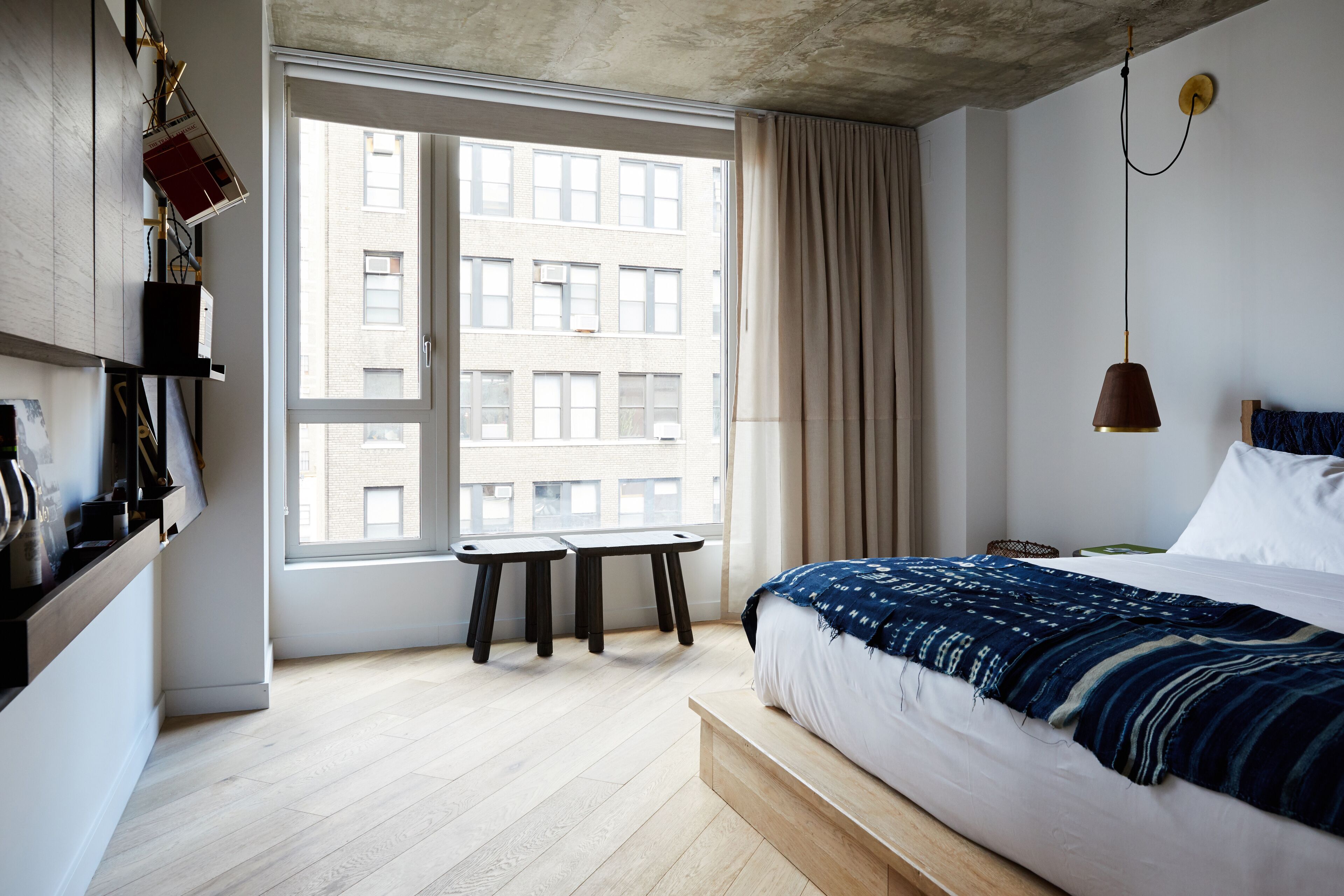 A modern bedroom with a large window, a bed with a blue blanket, and a small table by the window.
