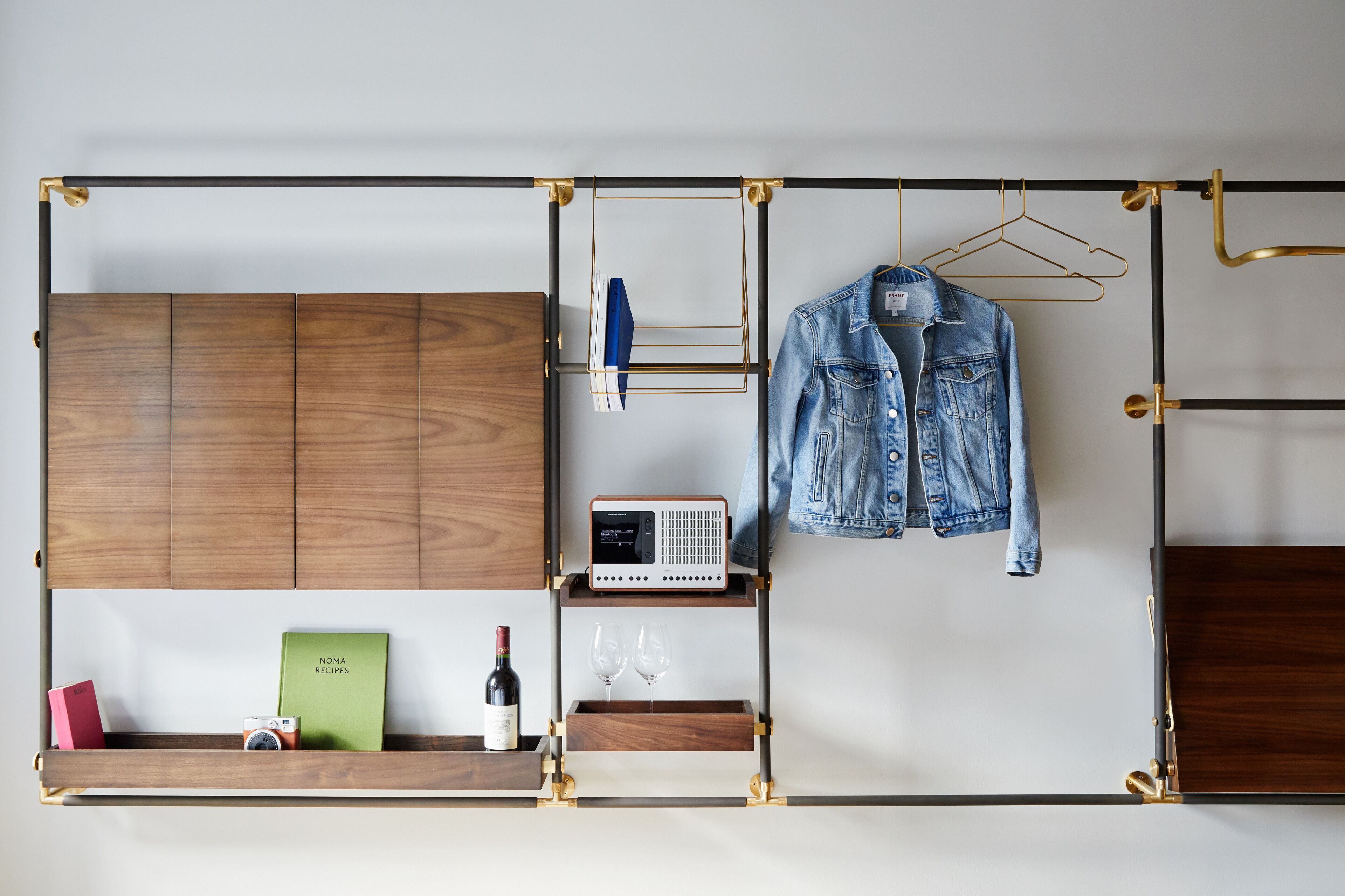 Ein Zimmer mit einem Holzschrank, einem Radio, einer Jeansjacke, einer Weinflasche und einem grünen Buch im Regal.