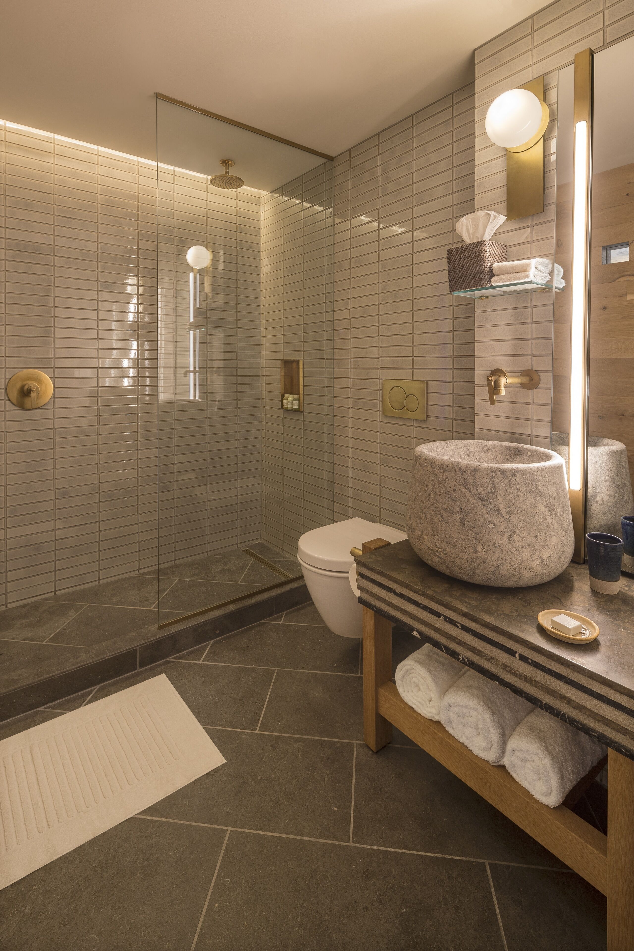 Un baño moderno con lavamanos de piedra, cabina de ducha de vidrio y tocador de madera.