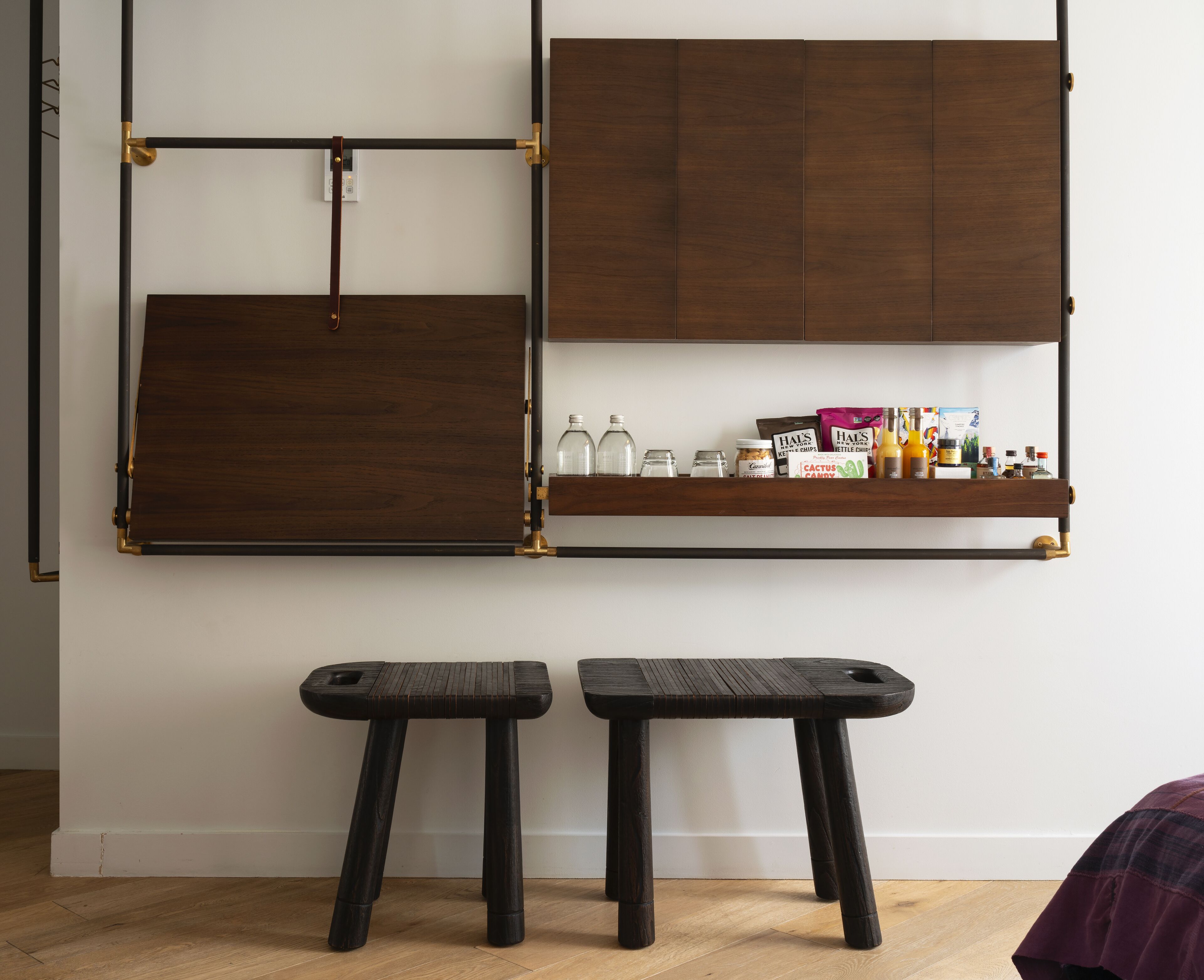 A room with a wooden cabinet, a shelf with various items, and two stools.