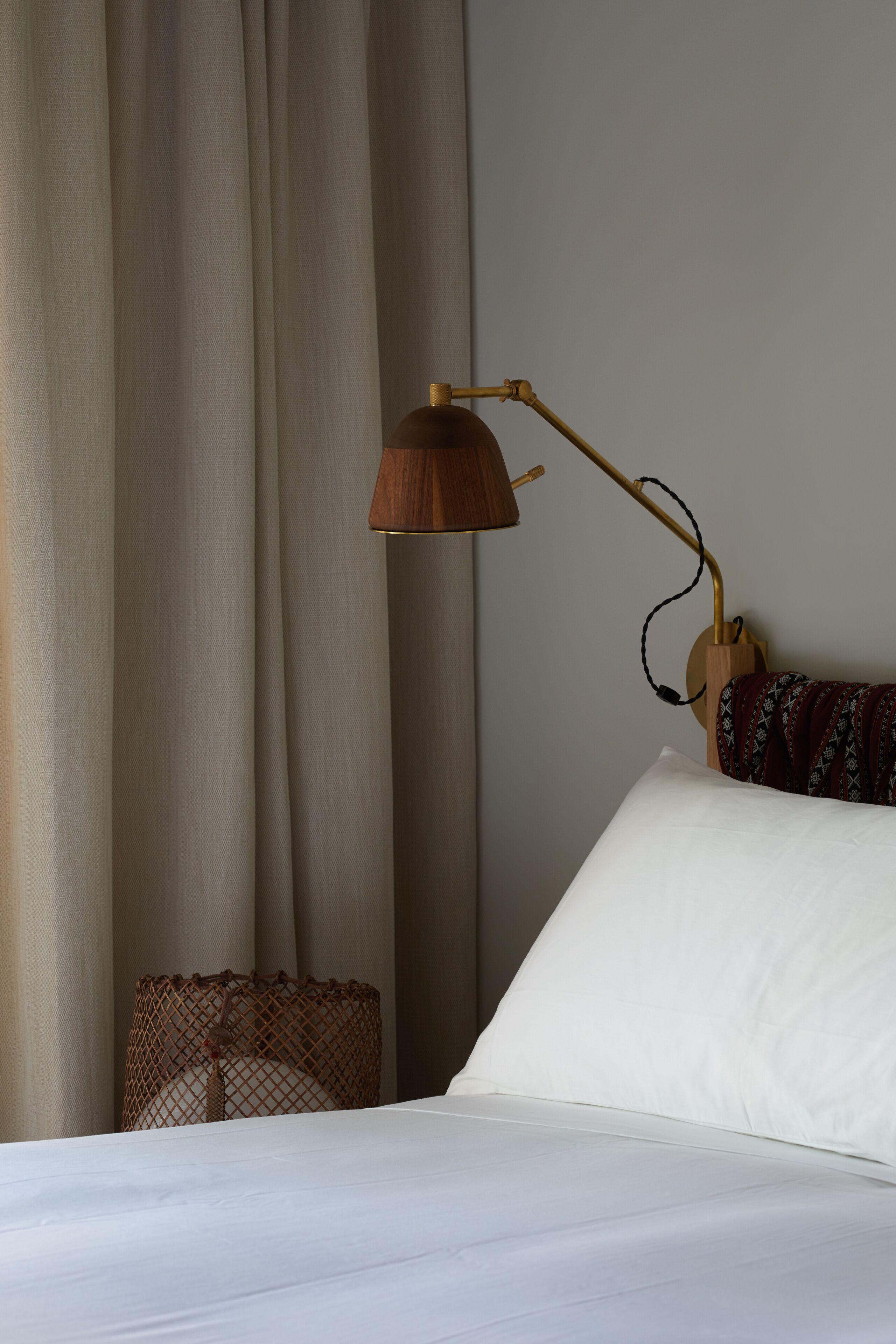 Una cama bien hecha con sábanas blancas, una mesita de noche de madera con una lámpara y una manta decorativa.