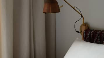 Una cama bien hecha con sábanas blancas, una mesita de noche de madera con una lámpara y una manta decorativa.