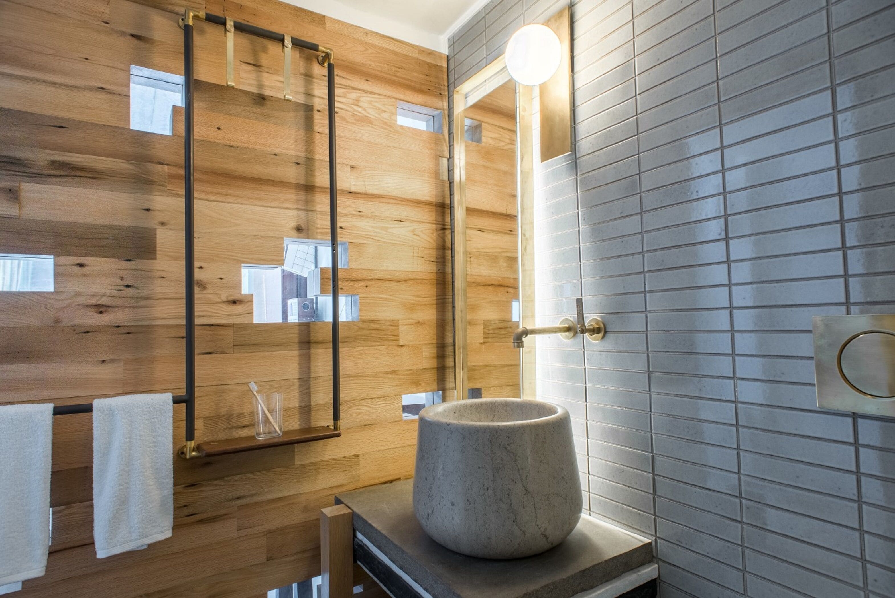 A modern bathroom with wooden paneling, a large mirror, a round stone basin, and a tiled wall.
