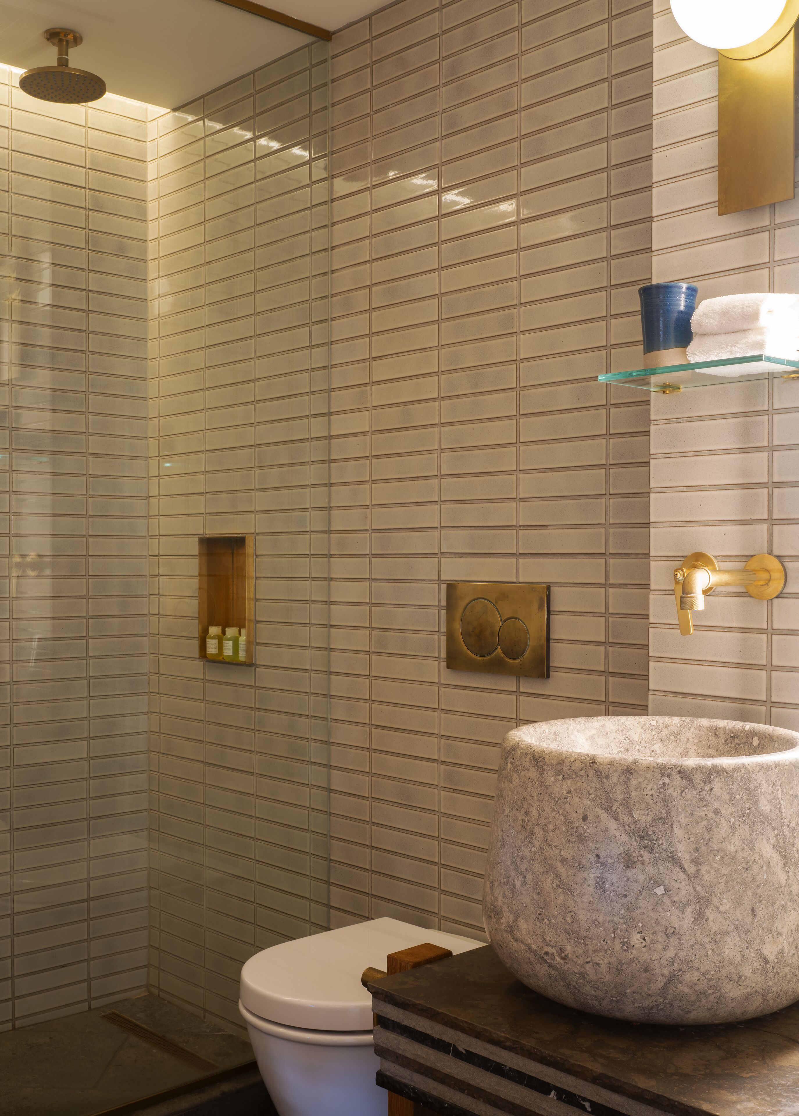 Un baño moderno con un lavamanos de piedra grande, un estante de vidrio y una zona de ducha.