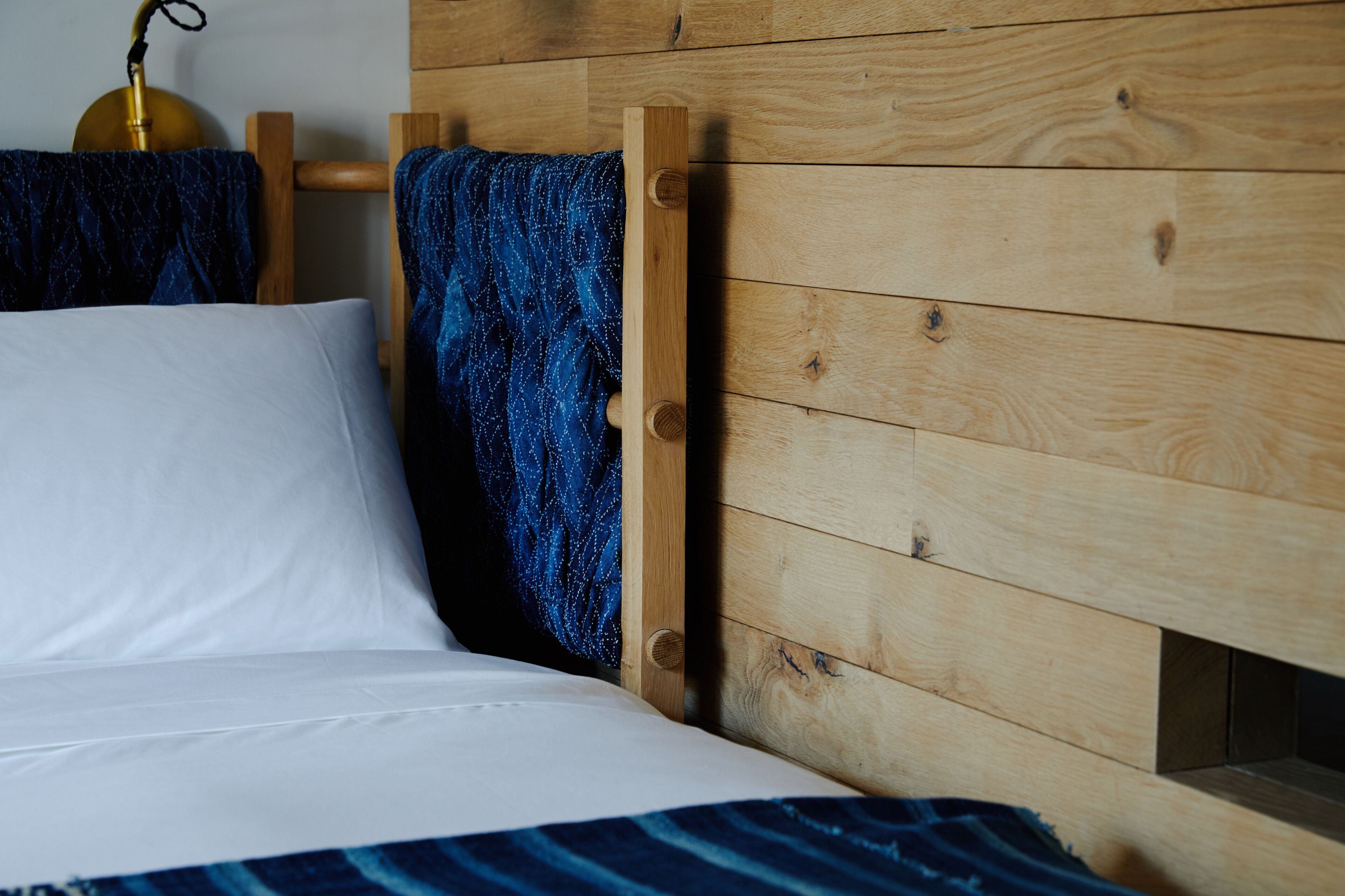 Ein Bett mit weißer Bettwäsche, einem Holz-Kopfteil und einer blauen, gemusterten Decke.