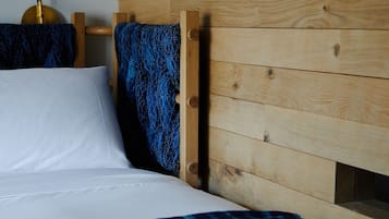 Ein Bett mit weißer Bettwäsche, einem Holz-Kopfteil und einer blauen, gemusterten Decke.