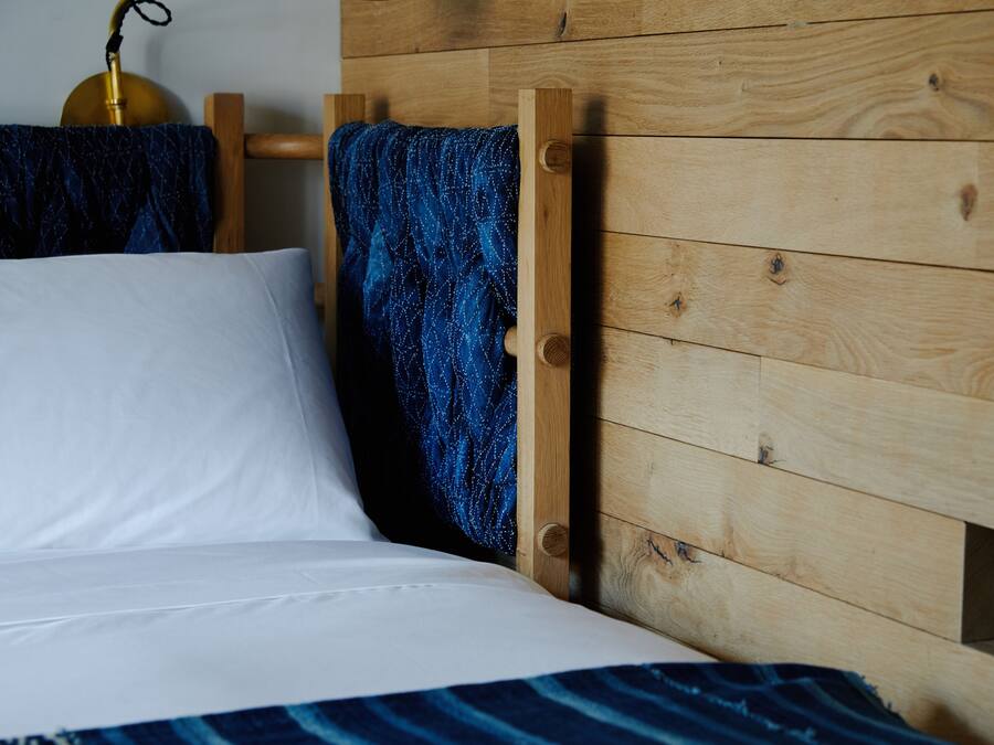 Una cama con ropa blanca, un cabecero de madera y un plaid azul estampada.