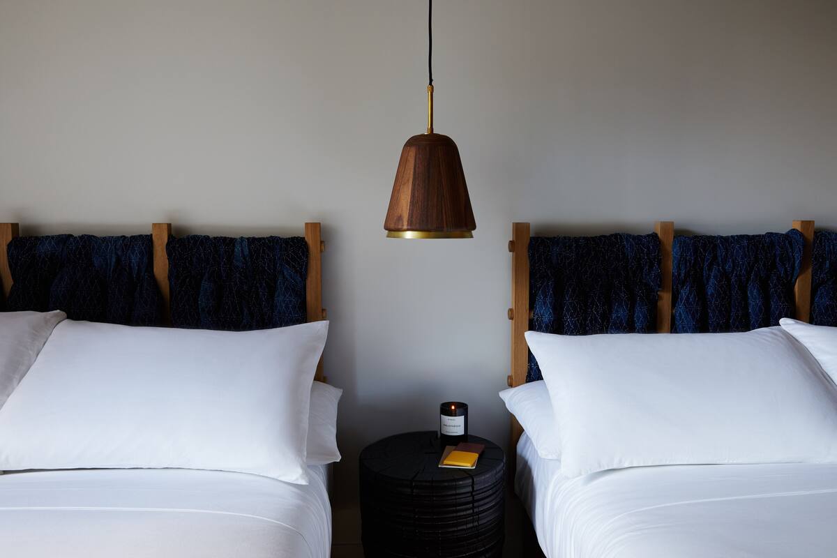 Habitación de hotel con dos camas, una mesita de noche redonda negra con una vela, y una lámpara colgante.