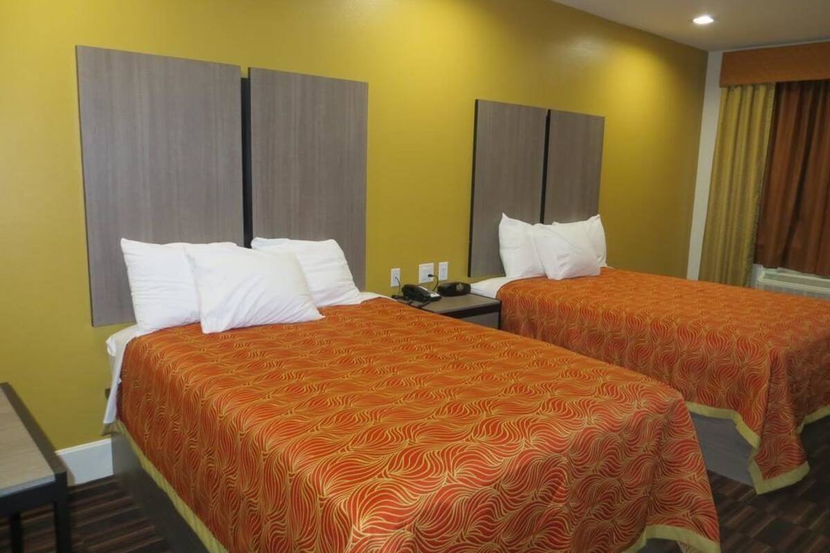 A hotel room with two beds, each with a patterned bedspread and white pillows.