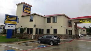 Edifício do Scottish Inn & Suites com estacionamento e um carro na frente.