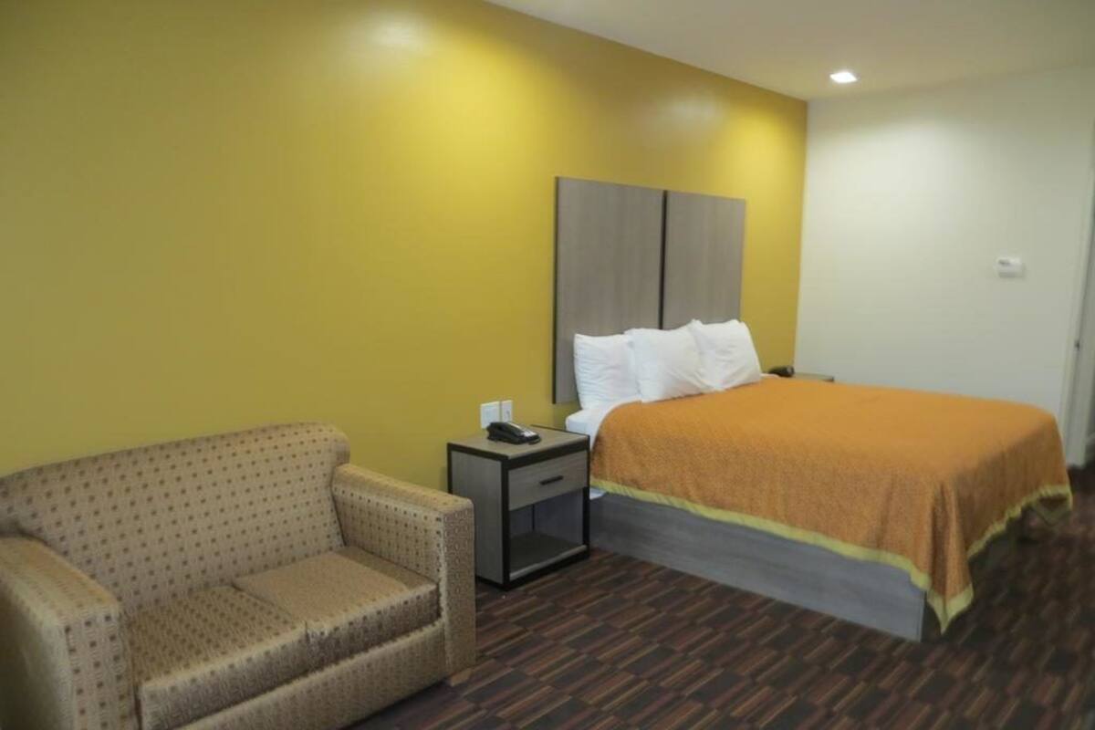 A hotel room with a bed, a sofa, a nightstand, and a telephone.