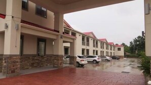 Hotel com galeria coberta, vários andares e carros estacionados.