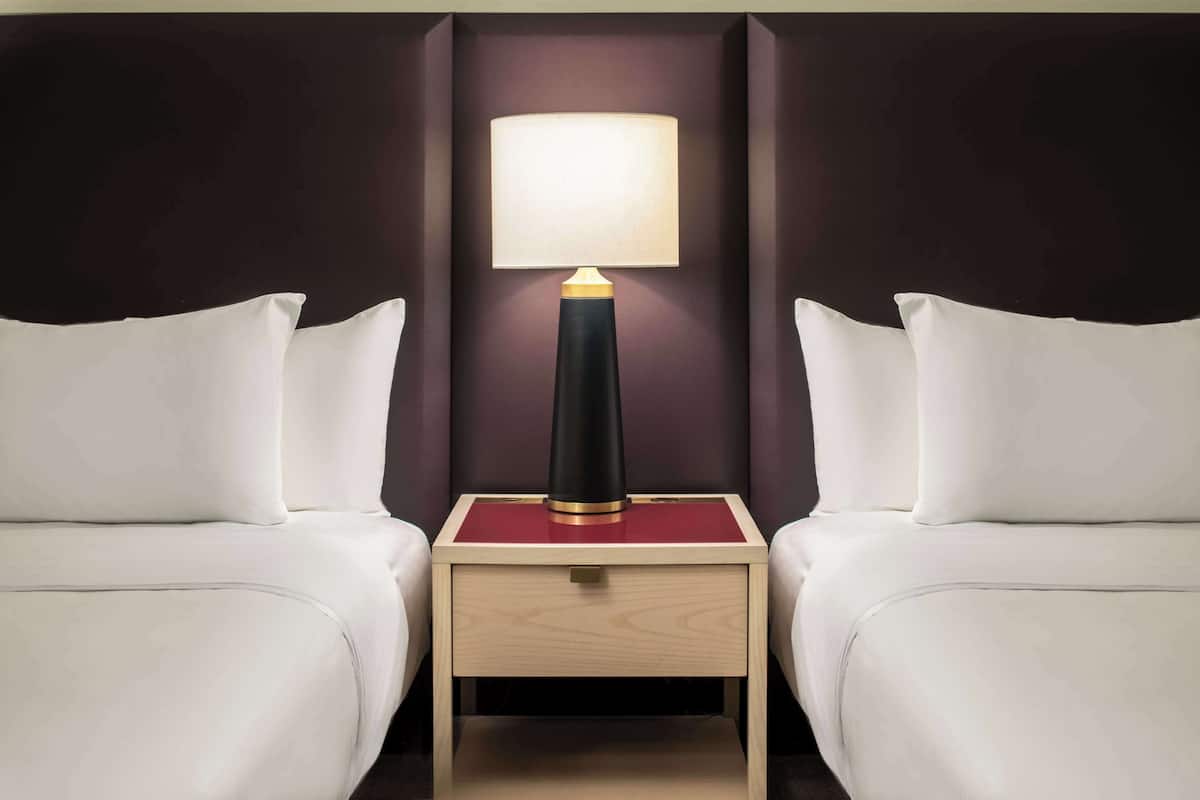 Une chambre d’hôtel avec deux lits, une table de chevet avec une lampe et un mur de couleur sombre.