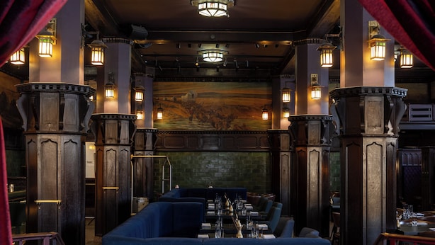 A restaurant with a blue booth seating area, wooden pillars, and hanging lantern-style lights. - Hotel Savoy Kansas City, Tapestry Collection by Hilton (Kansas City)