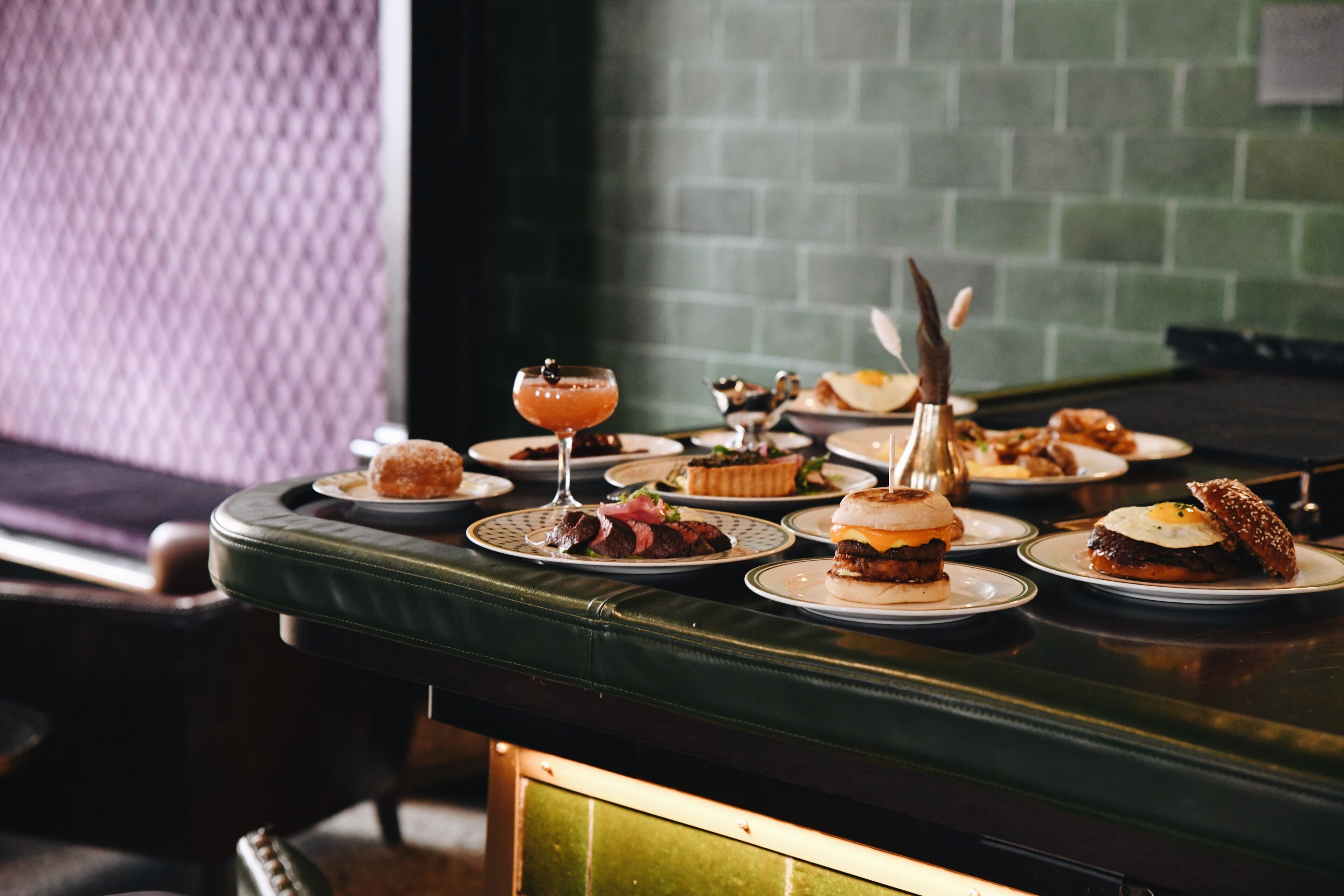 A bar area with a green cushioned bench and a variety of food and drink items on a table.