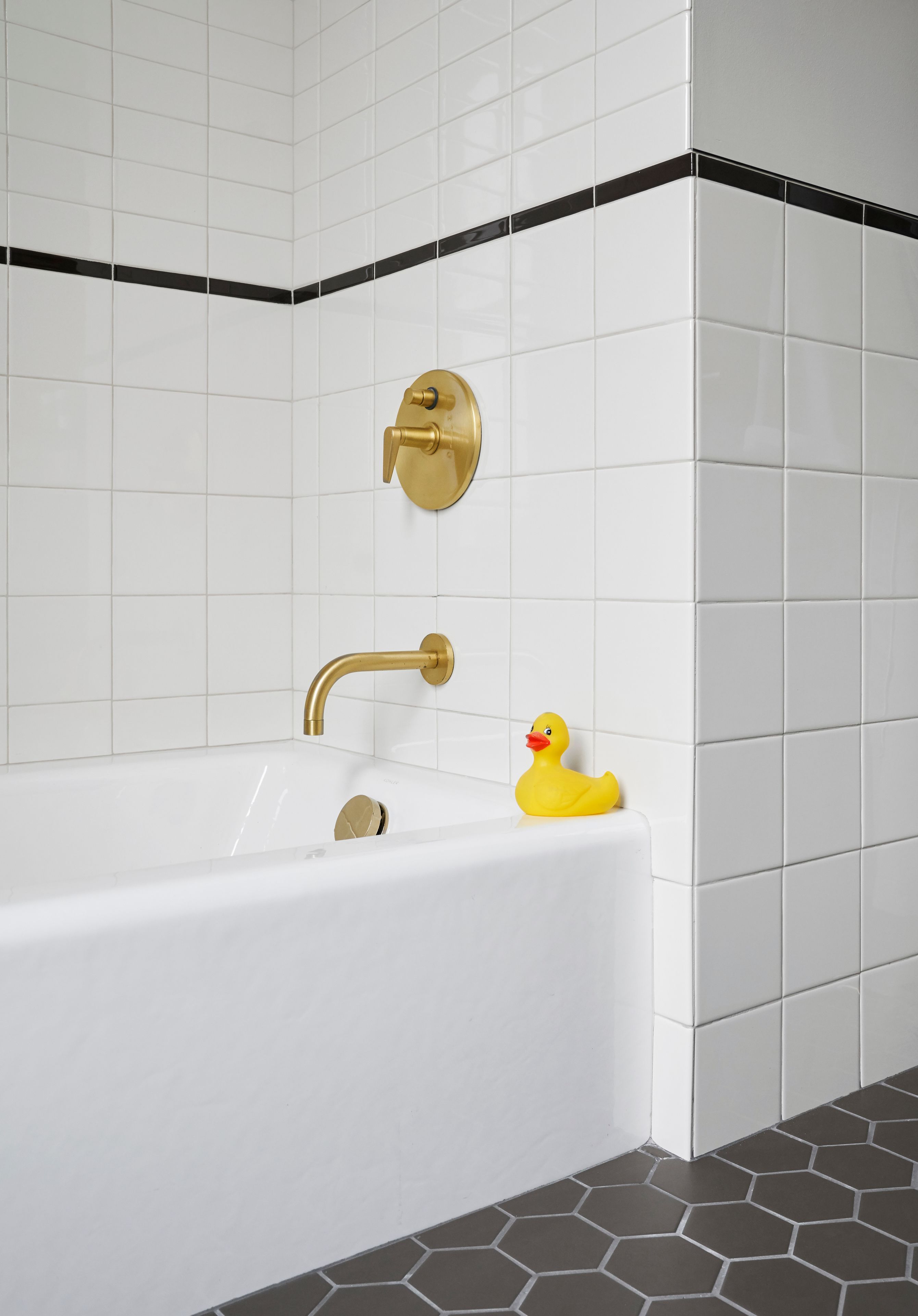 Een moderne badkamer met een witte badkuip, gouden details en een gele rubberen eend.