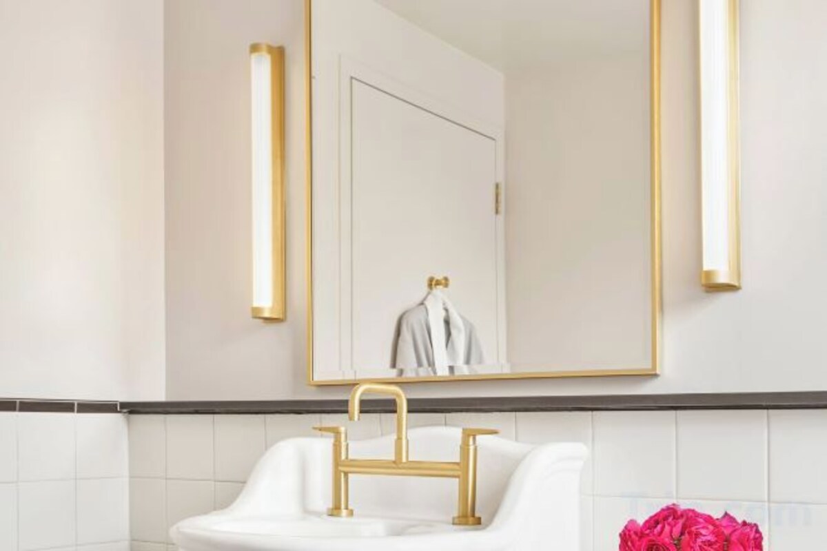 A bathroom with a white sink, gold faucet, and a large mirror with gold frame.