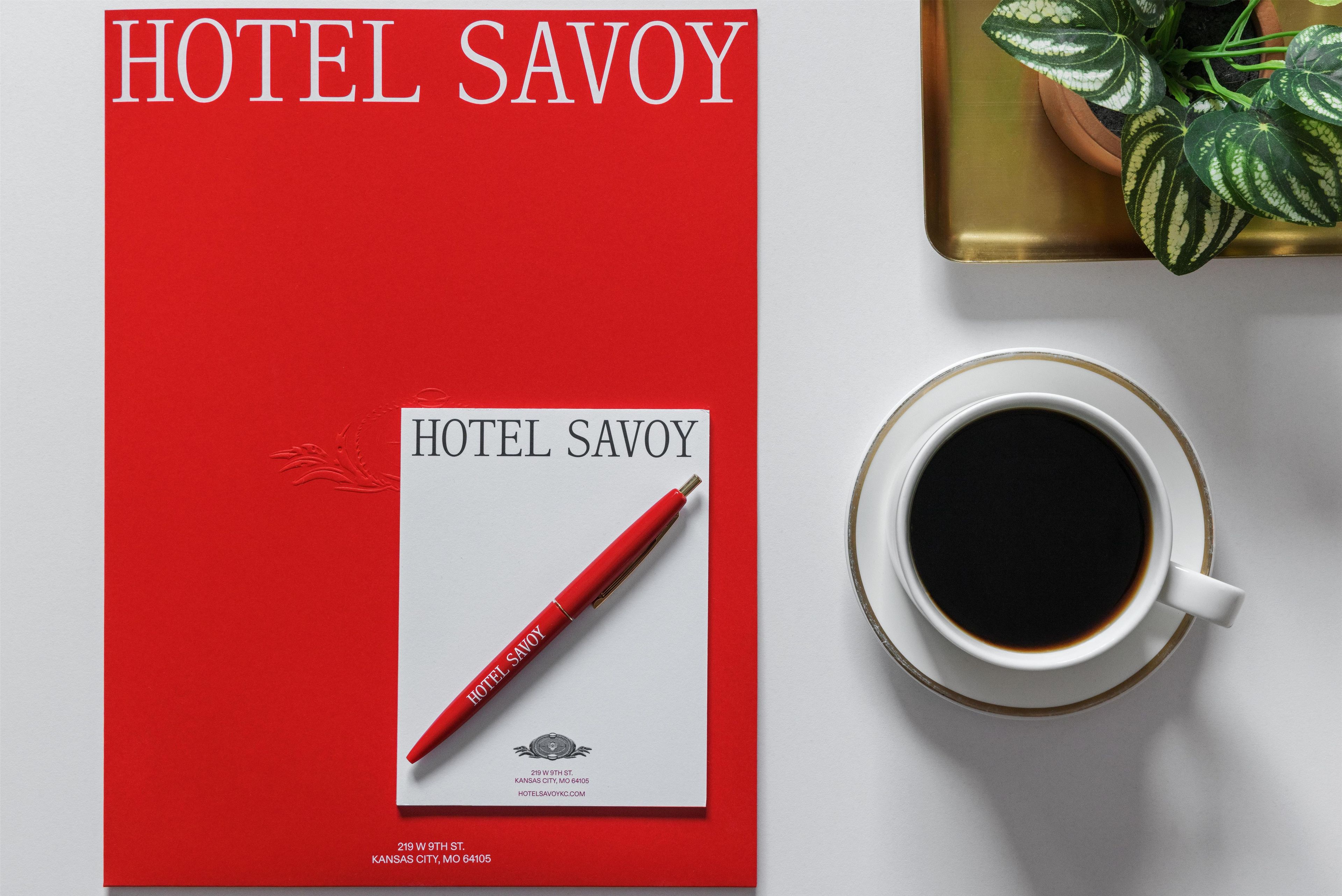 Eine rote Broschüre für das Hotel Savoy mit einem Stift und einer Kaffeetasse auf einem Tisch.