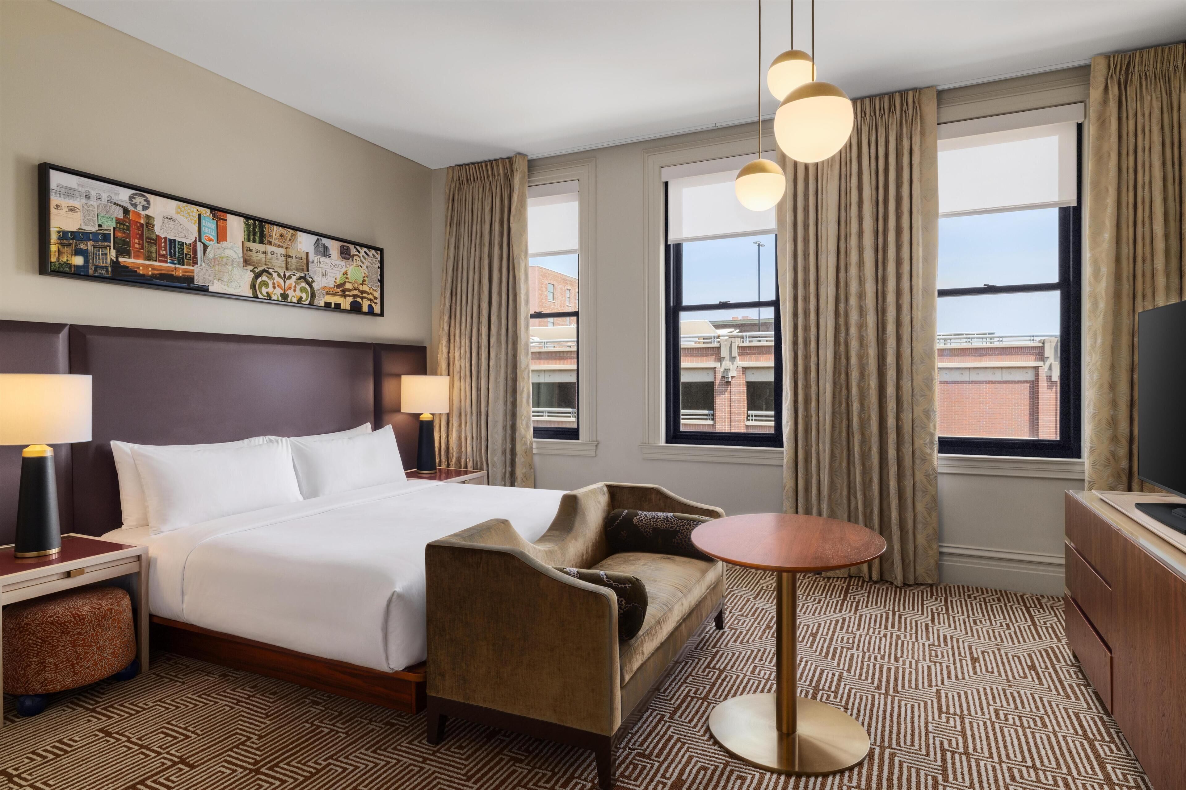 Habitación de hotel con cama, sofá, una mesita, televisor y un cuadro en la pared.